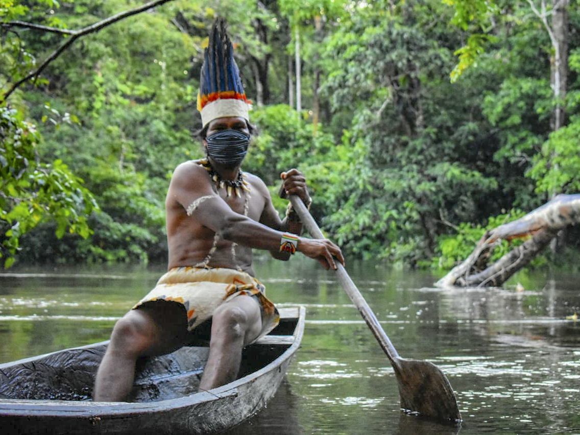 caption: A Colombian Huitoto man sails on a raft along the Takana river in Leticia, Amazonas department, Colombia, on May 20, during the coronavirus pandemic.