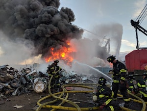 caption: Seattle firefighters tackle a blaze amid scrapped cars along the Duwamish River on June 26.