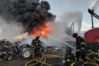 caption: Seattle firefighters tackle a blaze amid scrapped cars along the Duwamish River on June 26.