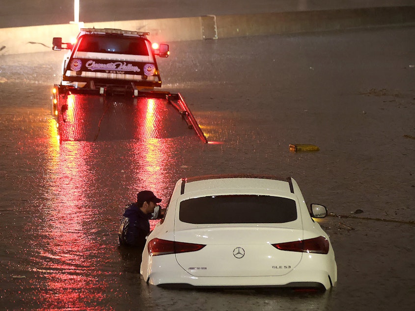 caption: A tow truck driver attempts to pull a stranded car out of floodwaters on the Golden State Freeway as tropical storm Hilary moves through the area on August 20, 2023 in Sun Valley, California.