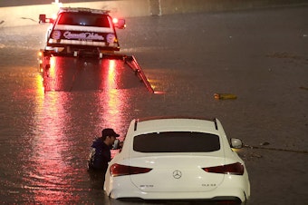 caption: A tow truck driver attempts to pull a stranded car out of floodwaters on the Golden State Freeway as tropical storm Hilary moves through the area on August 20, 2023 in Sun Valley, California.