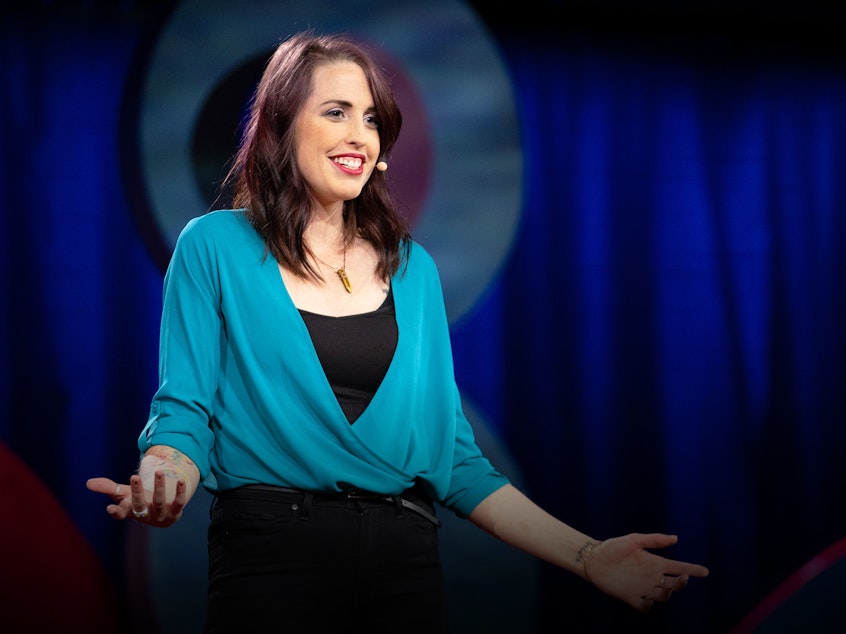 caption: Emily Quinn speaks from the TED stage at TEDWomen 2018