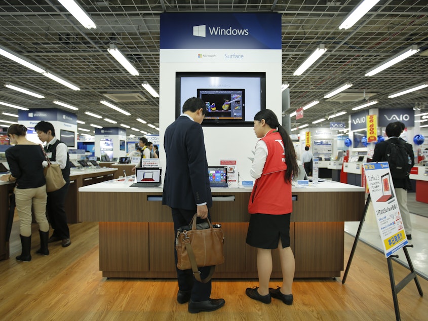caption: Microsoft's division in Japan says it saw productivity grow by 40% after allowing employees to work for four days a week rather than five. In this file photo, a sales clerk speaks with a customer in front of Microsoft Corp.'s display at an electronics store in Tokyo.