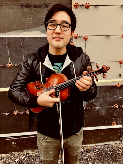 caption: Joe Kye stands for a portrait with his violin in the University District. 