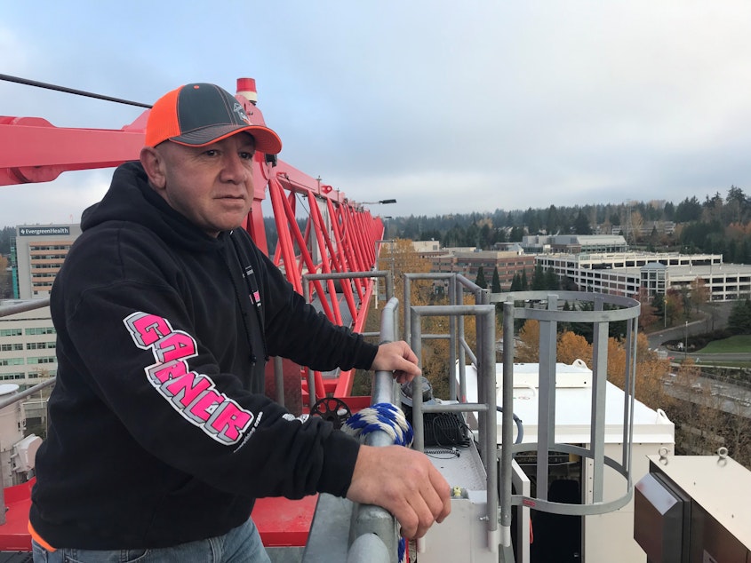 caption: Bruce Tamblin stands at the top of his crane at a construction site in Kirkland. He has been putting holiday lights on his crane for over a decade. 