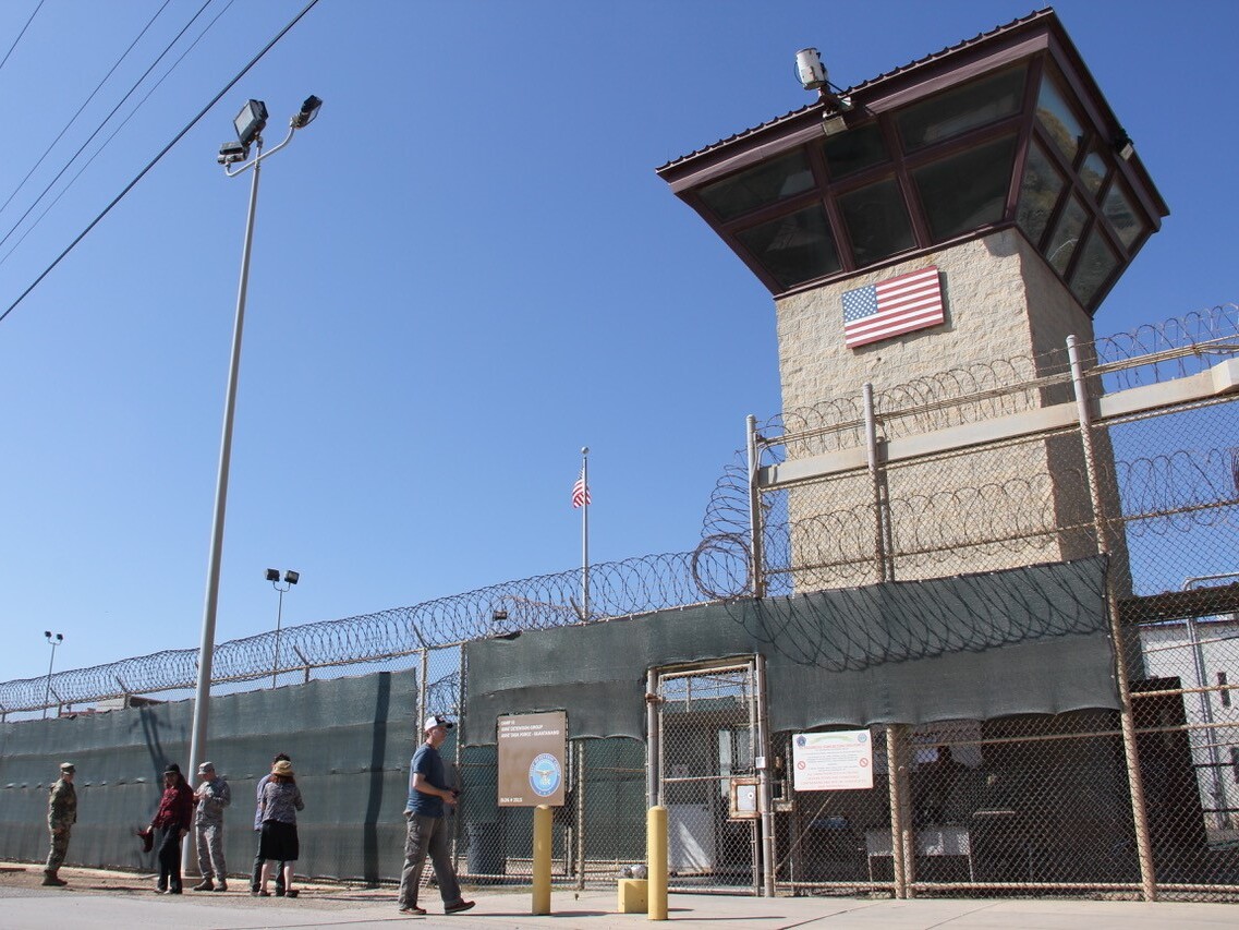 caption: People walk past a guard tower outside the fencing of Camp 5 at the the U.S. military's prison in Guantánamo Bay, Cuba, on Jan. 26, 2017.