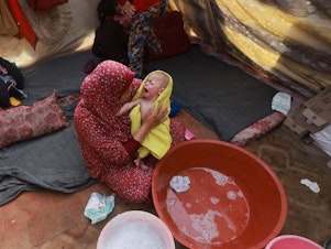 caption: A woman dries a baby in a towel after giving the infant a bath inside a tent at a camp for displaced Palestinians in Rafah, in southern Gaza, on Jan. 18.