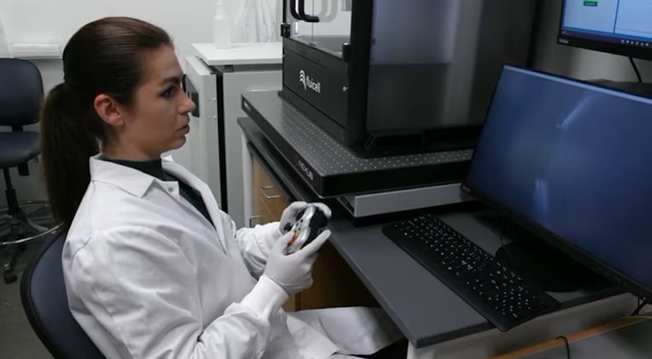 caption: Oregon Health and Science University researcher Haylie Helms uses a video game controller to direct a 3D printer head and precisely print individual cells in this image collected from "All Science. No Fiction." video footage in October 2023.