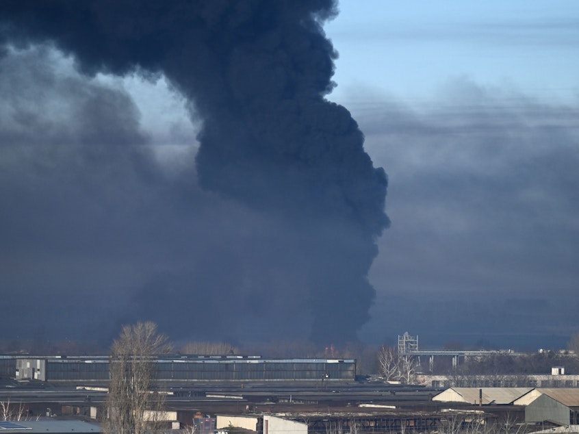 caption: Black smoke rises from a military airport in Chuhuiv, near Kharkiv, Ukraine, on Thursday. Humanitarian organizations say Russian forces are using cluster munitions in their bombing and shelling of Ukraine.