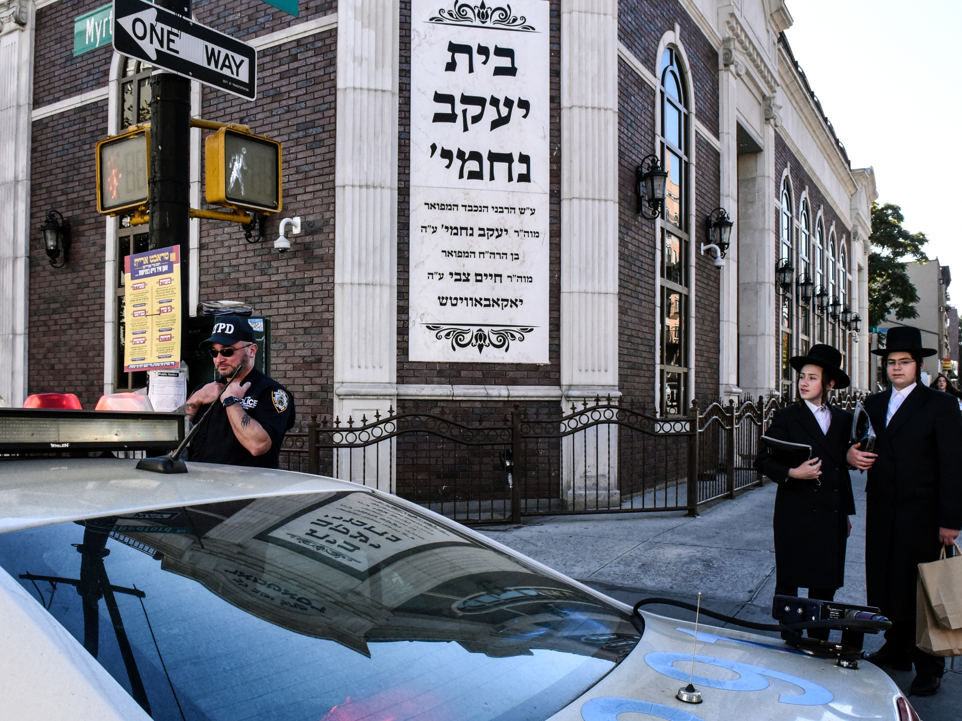 caption: A member of the New York Police Department patrols in front of the synagogue Congregation Bais Yaakov Nechamia Dsatmar on Oct. 13, 2023 in the Williamsburg neighborhood in the borough of Brooklyn in New York City.