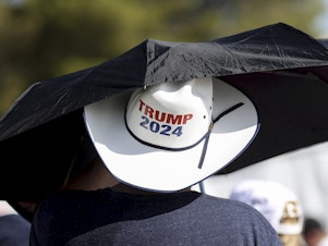 caption: A man uses an umbrella at a campaign rally for former President Donald Trump on June 9 in Las Vegas, where temperatures climbed above 100 degrees. 
