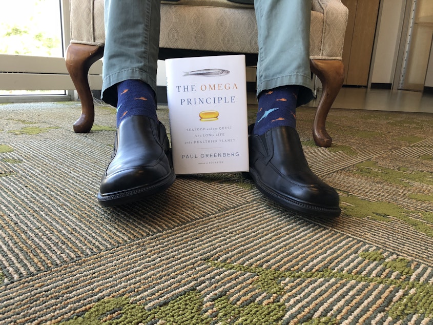 caption: Paul Greenberg shows off this fish socks and his new book at the KUOW studios
