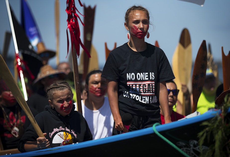 caption: Rosalie Fish, 18, requests permission to come ashore in a Cowlitz tribal canoe after a multi-day canoe journey on Wednesday, July 24, 2019, during Paddle to Lummi at the Lummi Nation Stommish Grounds. A red painted hand print over her mouth honors missing and murdered indigenous women. "The purpose of the paint here today is to show a symbol of unity and to say that my canoe family stands with the relatives that have been affected by this epidemic," Fish said. 