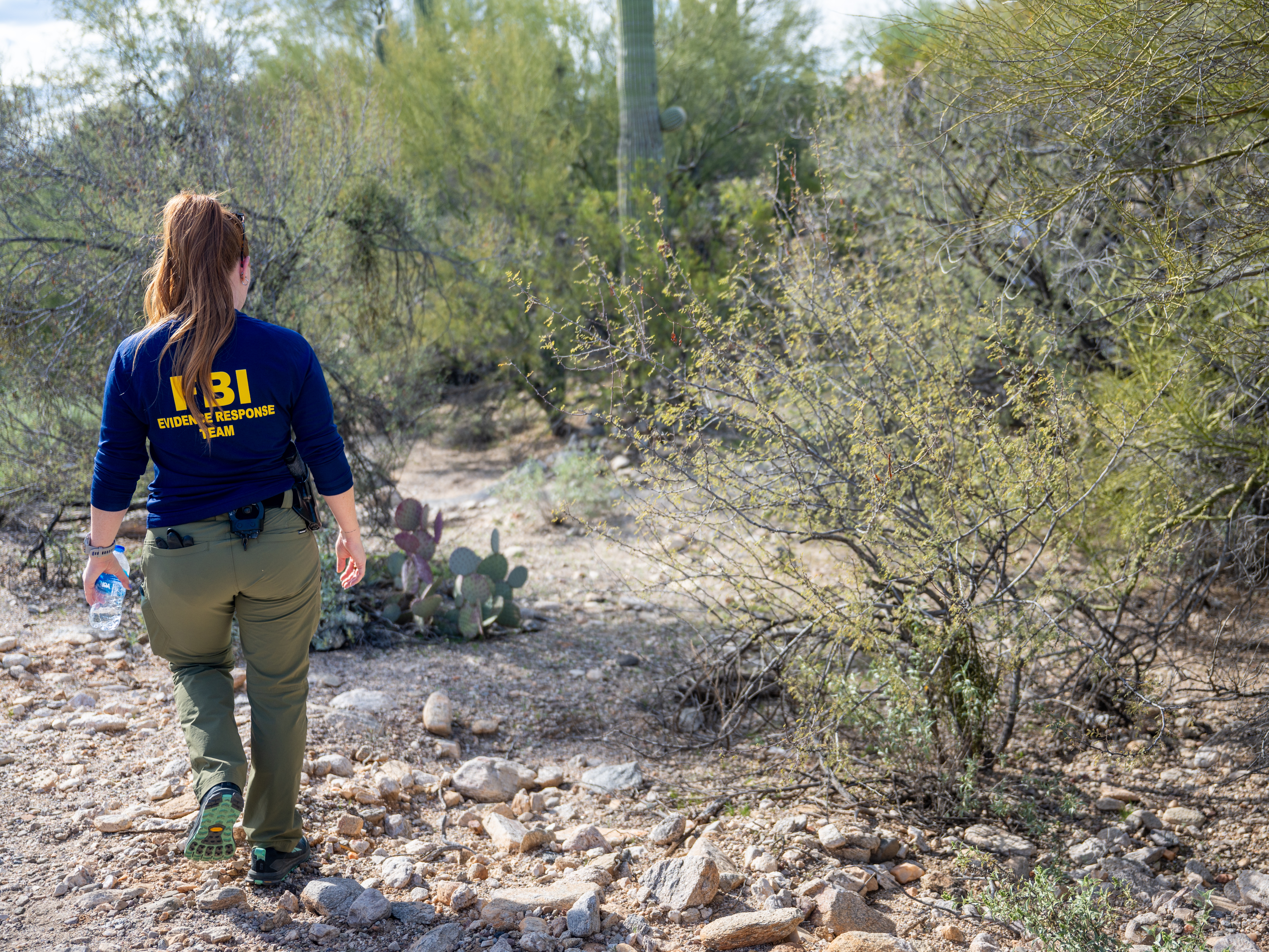 caption: A member of the FBI's Evidence Response Ream searches an area around Nancy Guthrie's residence in Tucson, Ariz., on Feb. 11. Police say that DNA samples have been recovered in and around Guthrie's home and that investigators are considering "additional investigative genetic genealogy options."