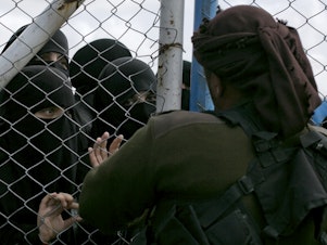 caption: In this March 31, 2019, photo, women speak to guards at the gate that closes off the section for foreign families who lived in the Islamic State's so-called caliphate, at al-Hol camp in Hasakeh province, Syria.