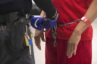caption: A guard prepares to handcuff a detainee on Tuesday, Sept. 10, 2019, in the intake holding area of the Northwest ICE Processing Center, formerly known as the Northwest Detention Center, in Tacoma.