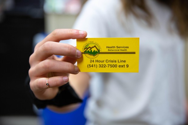 caption: <p>Sydney Wilkins holds a card for the 24-hour crisis line &mdash; she keeps it in her phone case.</p>