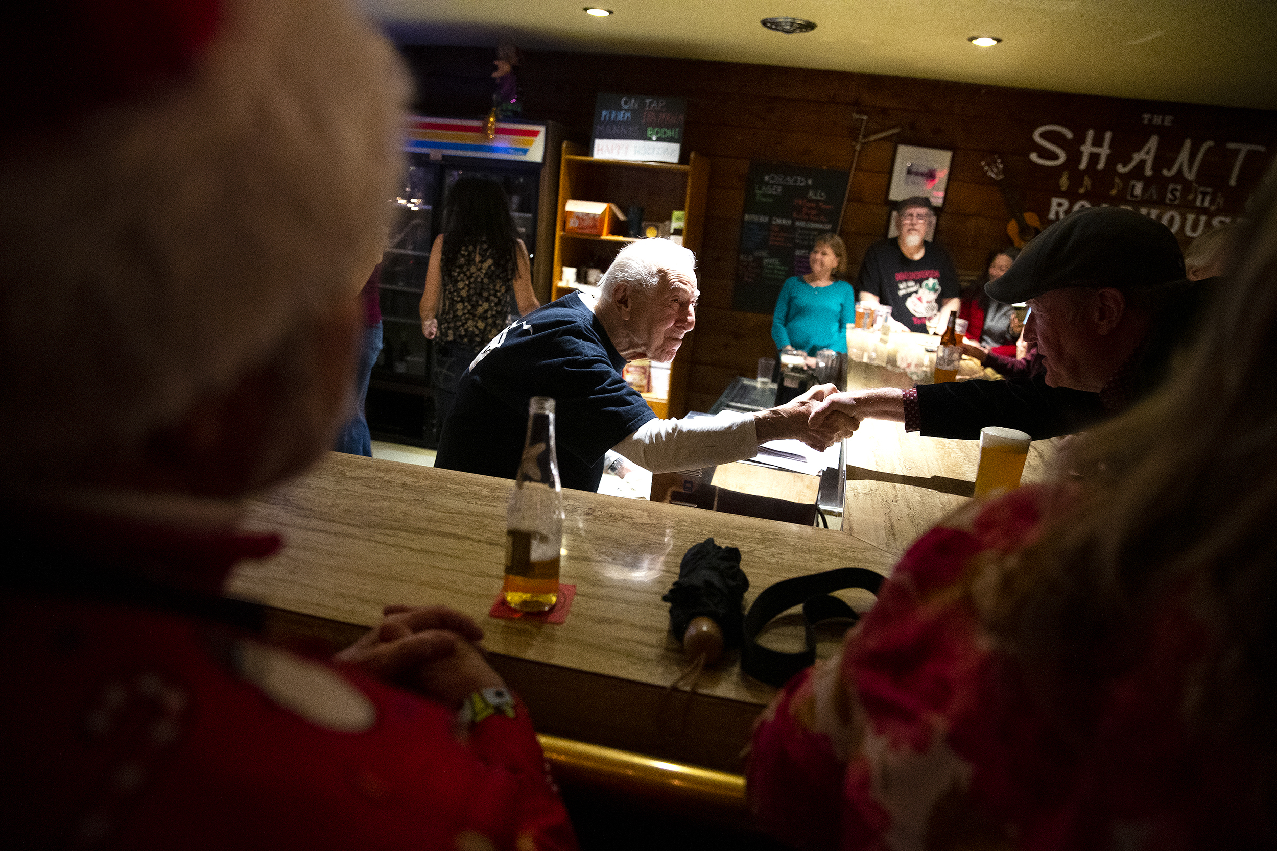 caption: John Spaccarotelli, 94-year-old owner and bartender at what many call the ‘last roadhouse in Seattle,’ shakes hands with a customer on Friday, December 19, 2025, during the last night of business at the Shanty Tavern in Lake City. 