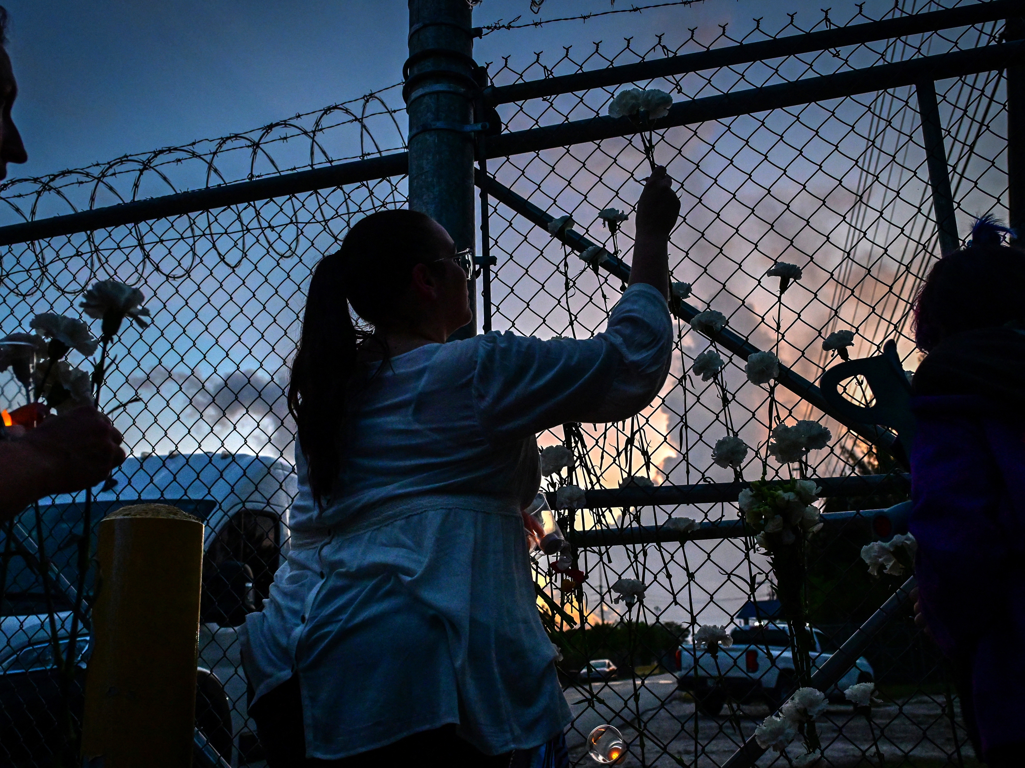 caption: People place white carnation flowers on the fence of the Krome Detention Center during a vigil protesting US Immigration and Customs Enforcement custody and mass deportations in Miami on May 24, 2025.