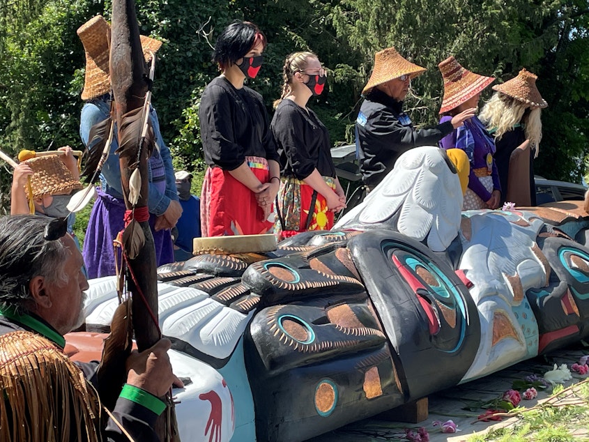 caption: Lead carver Jewell Praying Wolf James (left), known as Sit ki kadem, looks on while his brother Douglas James (center), known as Sit ki kadem, speaks to a large crowd on Orcas Island 