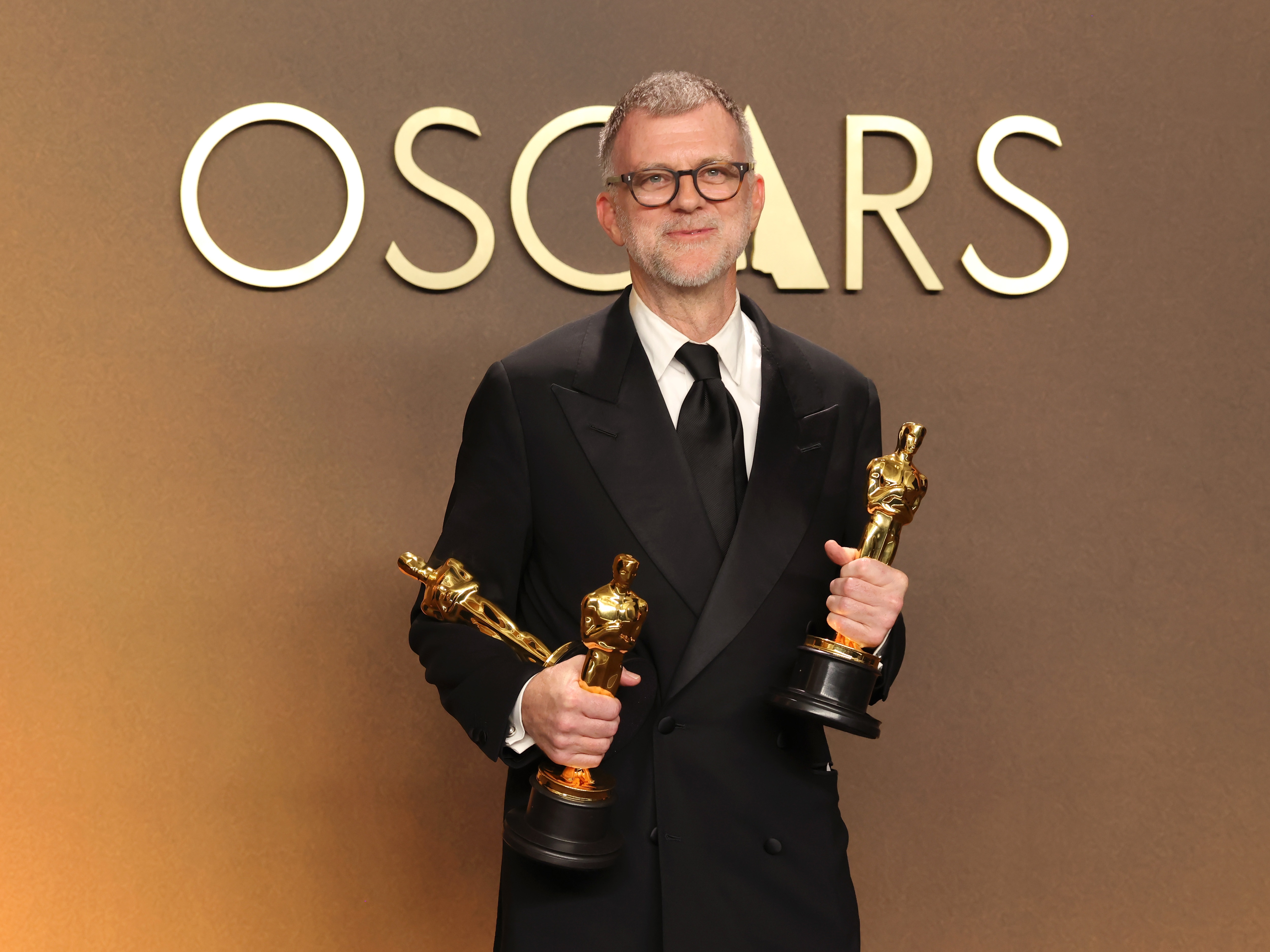 caption: Paul Thomas Anderson holds his Oscars for best adapted screenplay, best director and best picture for <em>One Battle After Another</em>.