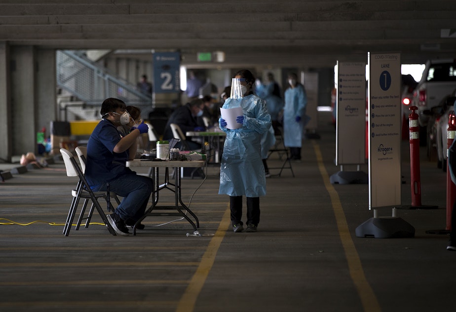 caption: FILE: QFC and Fred Meyer pharmacists are shown at a free drive-thru coronavirus testing site on Wednesday, May 13, 2020, in the parking garage at T-Mobile Park in Seattle. QFC and Fred Meyer announced a partnership with the city of Seattle and the Seattle Mariners for the free testing.