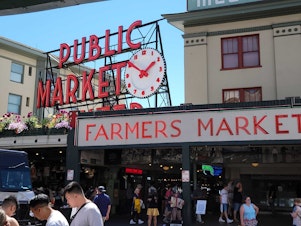 caption: Visitors stream through the main entrance to Pike Place Market in August 2022. 