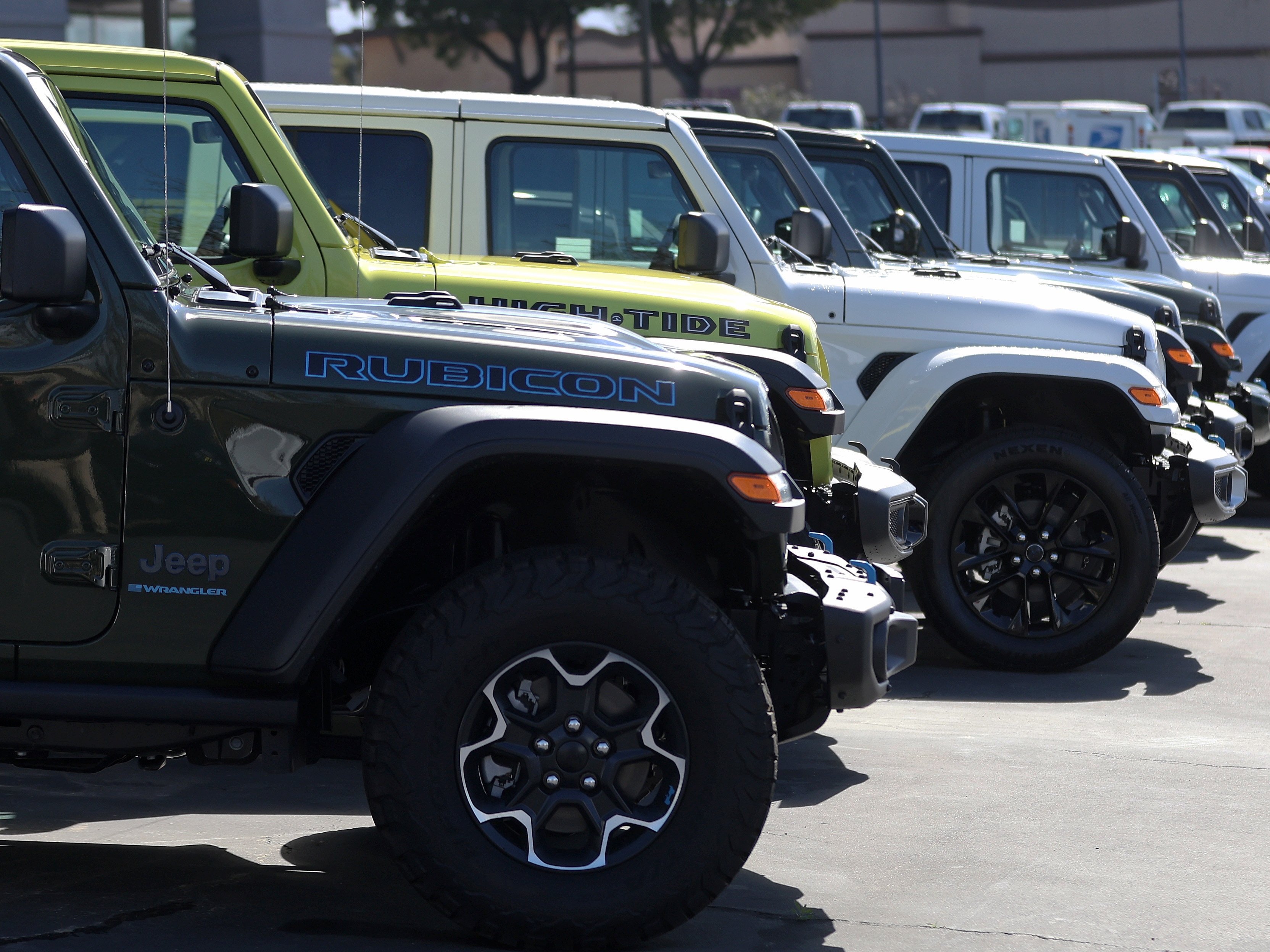caption: Jeep Wrangler 4Xe plug-in hybrids displayed on the sales lot at Hilltop Chrysler Jeep Dodge Ram in Richmond, California.