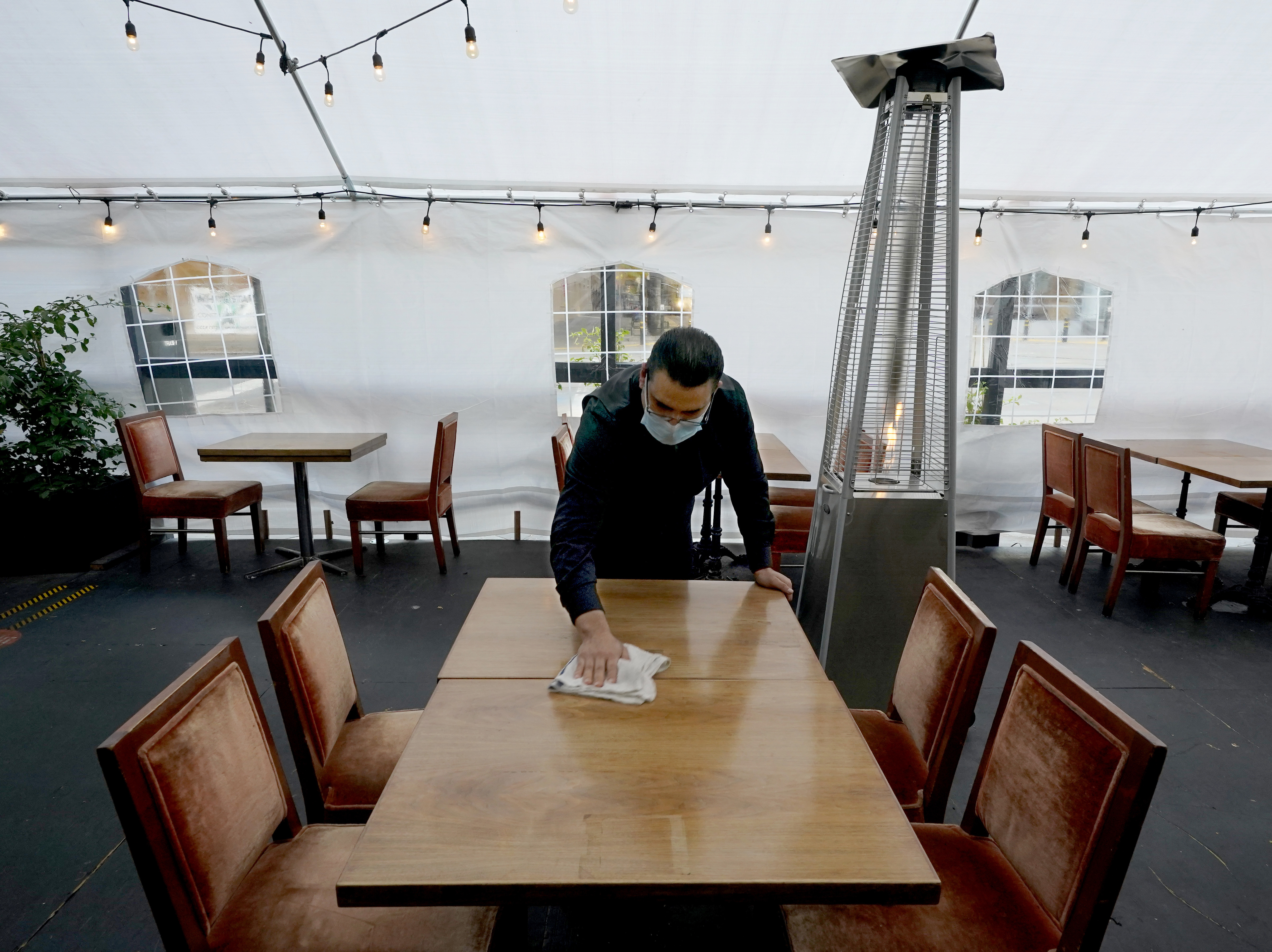 caption: A person cleans a table in an outdoor tented dining area of a restaurant in Sacramento, Calif., on Nov. 19. Job growth slowed sharply in November as relief aid is due to expire at the end of the year.