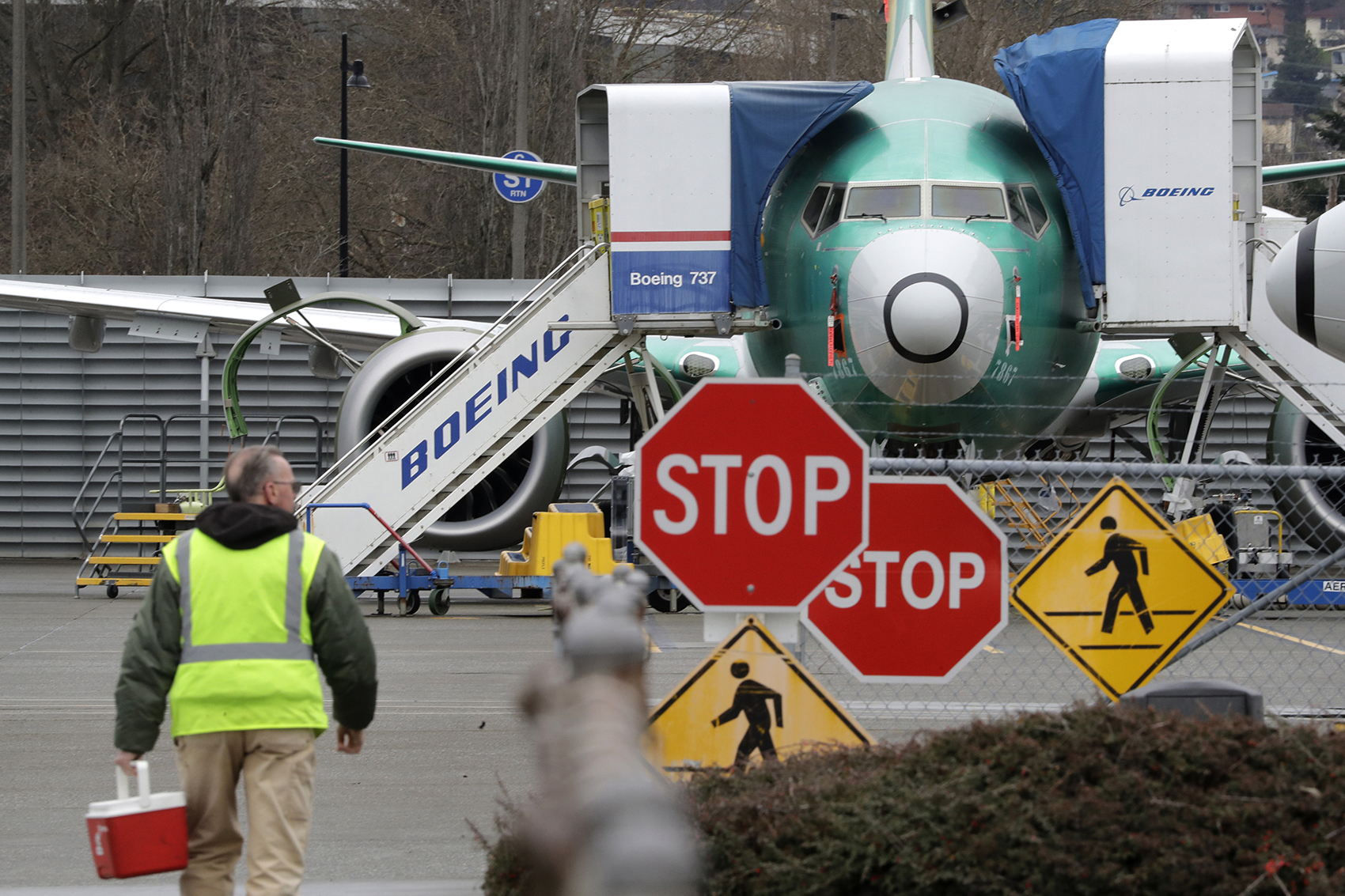 caption: In this Monday, Dec. 16, 2019, file photo, a Boeing worker walks in view of a 737 MAX jet in Renton, Wash. (Elaine Thompson, File/AP)