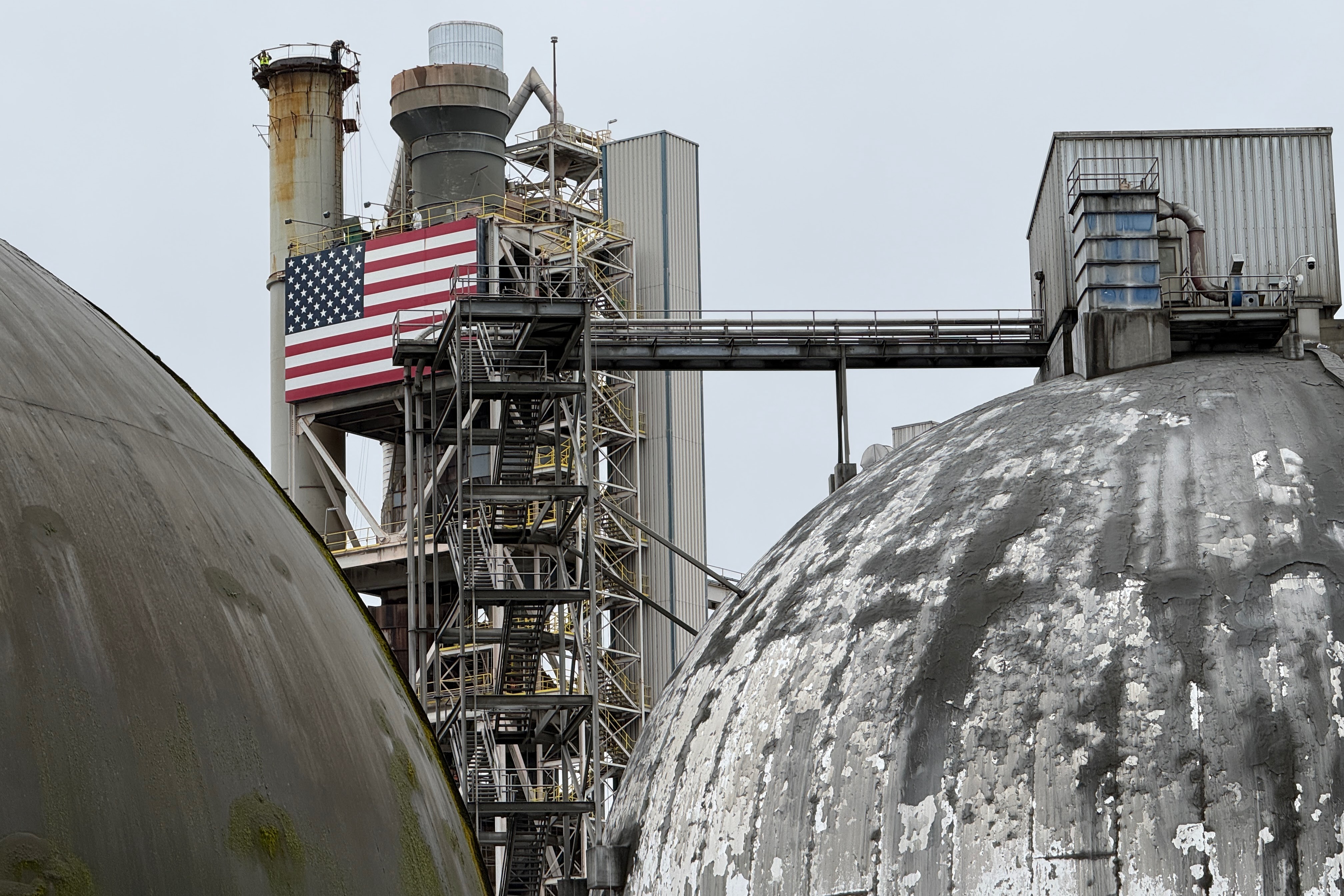 caption: Ash Grove Cement workers, barely visible, stand atop a cooling tower at the cement plant in Seattle on March 18, 2026.
