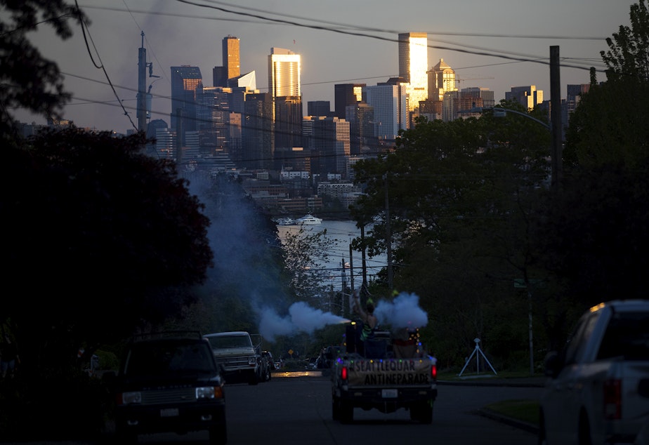 caption: The sun sets on downtown Seattle as the Seattle Quarantine Parade makes it's way through the Wallingford neighborhood on Friday, May 8, 2020, in Seattle.