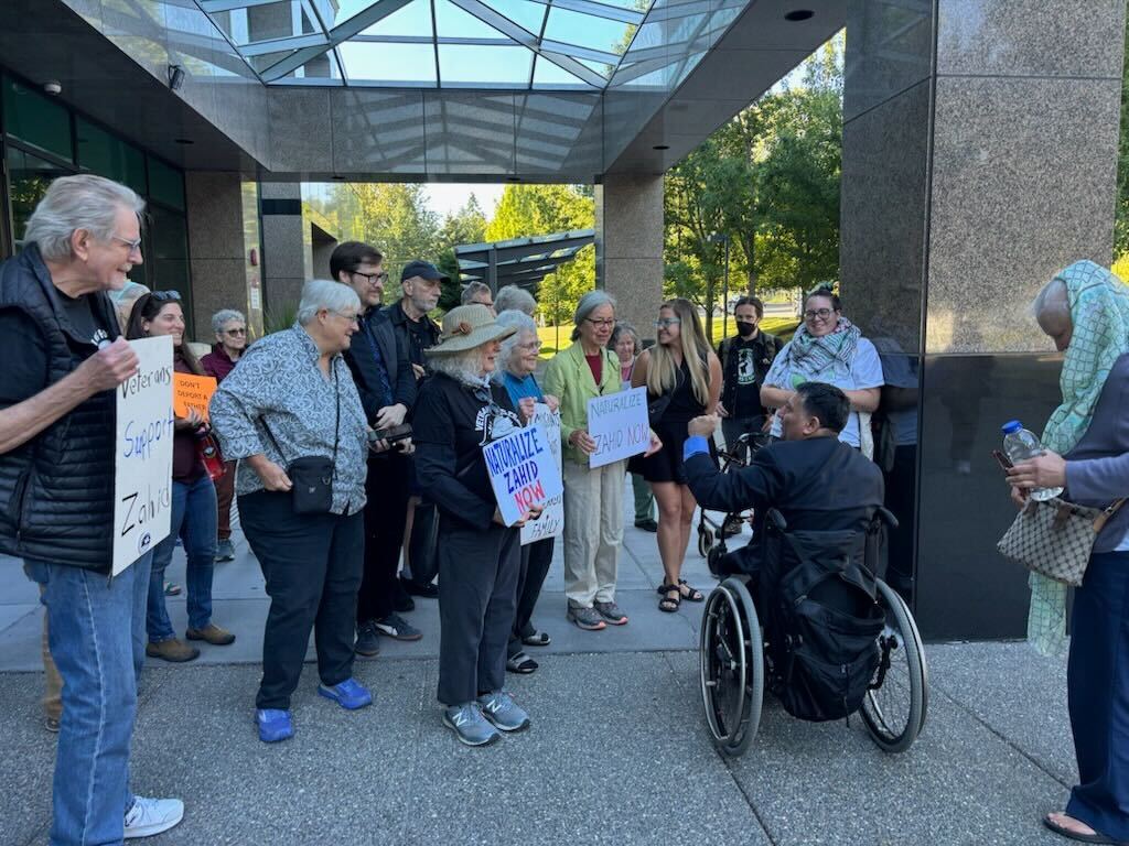 caption: Muhammed Zahid Chaudhry surrounded by friends, family, and supporters before he went into his citizenship hearing on Thursday, Aug. 22, 2025. 