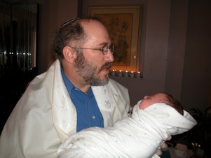 caption: Seattle mohel David Bolnick holds a baby following a bris ceremony.
