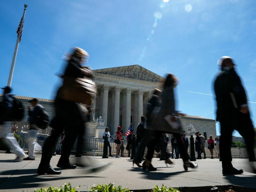caption: People walk by as supporters of Jan. 6 defendants gather outside of the Supreme Court on Tuesday.
