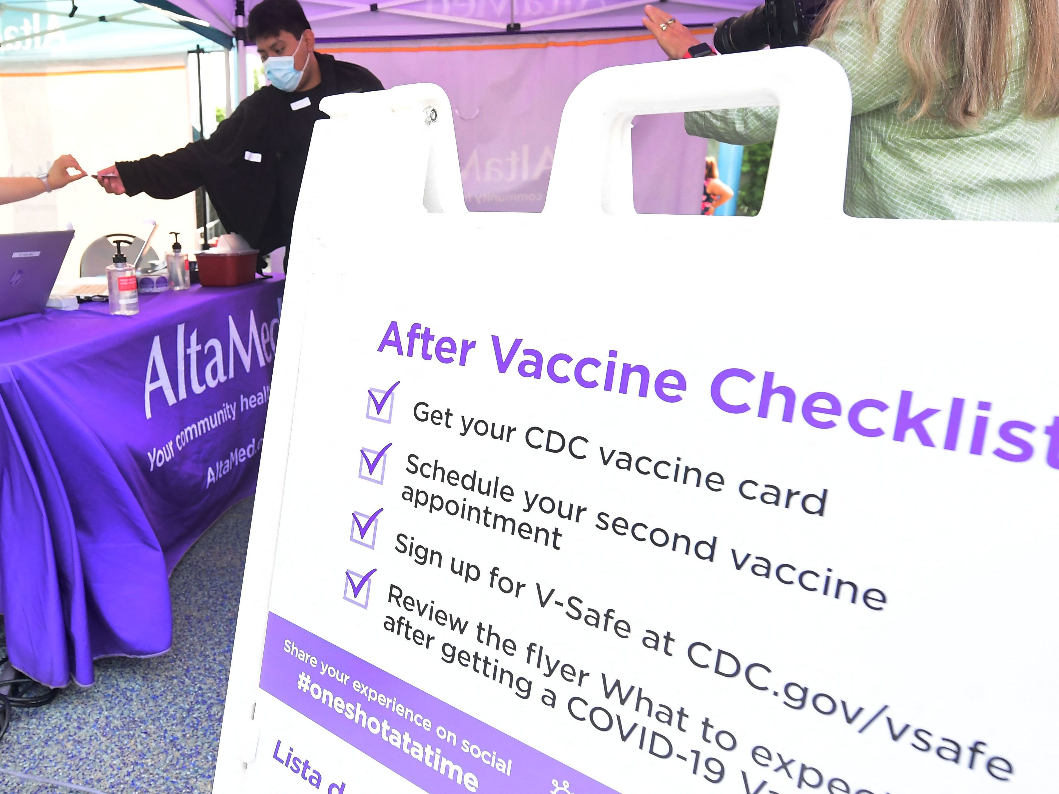 caption: A nurse from AltaMed Health Services hands out the vaccine card to people after receiving their Covid-19 vaccine in Los Angeles, California on August 17, 2021.