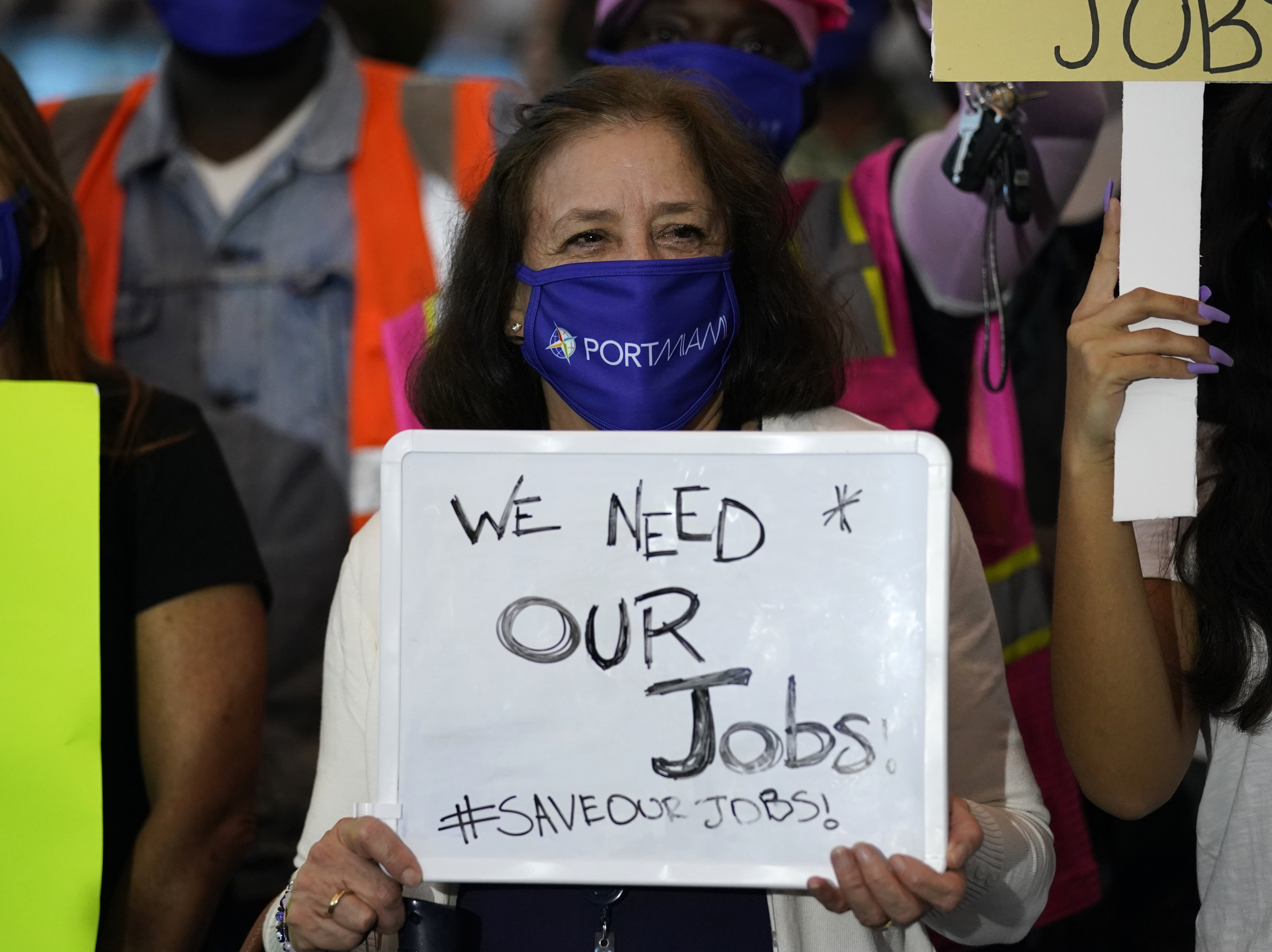 caption: A women holds a sign saying "We Need Our Jobs" during a protest by workers in the cruise ship industry in Miami on Oct. 21, 2020. Employers added fewer jobs as pandemic cases start to surge again across the country.