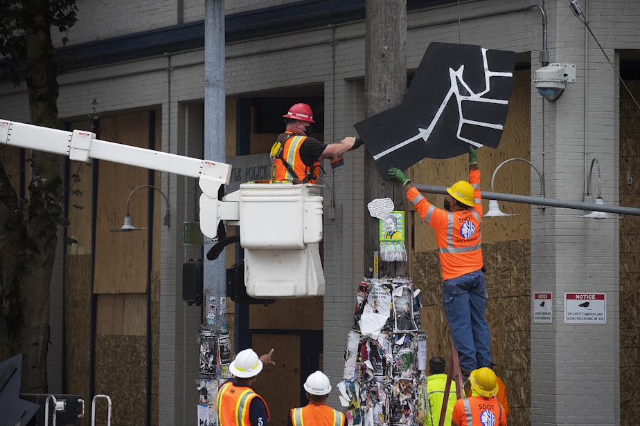 caption: Seattle Department of Transportation employees remove a Black power fist from a telephone pole outside of the East Precinct building after the Capitol Hill Organized Protest zone, CHOP, was cleared early Wednesday morning, July 1, 2020, in Seattle.