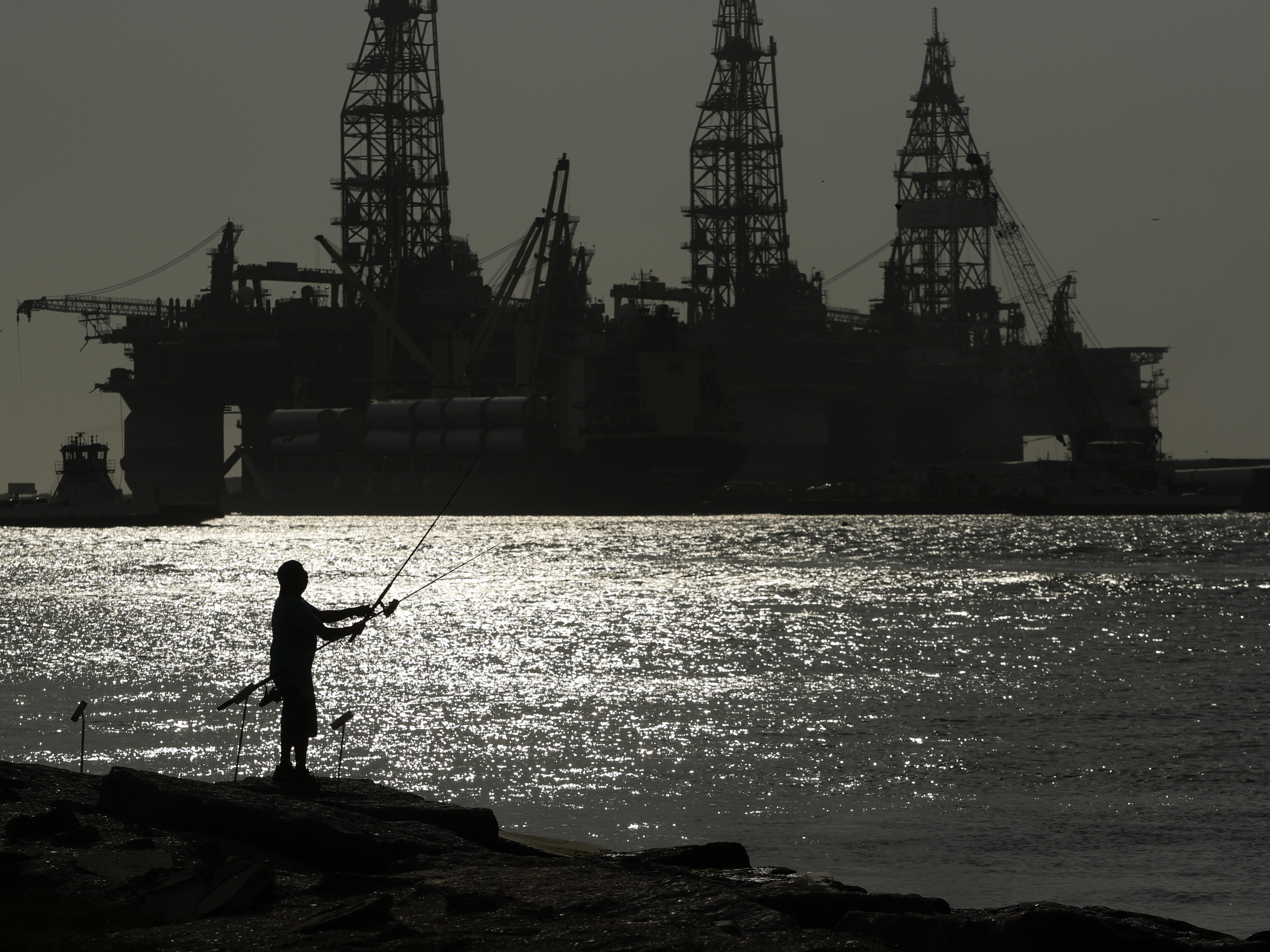 caption: A man fishes near docked oil drilling platforms in 2020 in Port Aransas, Texas. A federal judge has revoked oil and gas leases sold in the Gulf of Mexico in November, saying the Interior Department did not take into account its impact on climate change.