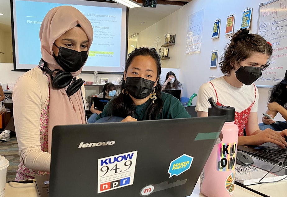 caption: Sadeen Al Ziyad (left) and Dashiell Pinck (right) work on their RadioActive stories with the support of mentor Dayana Capulong (center) in the RadioActive programming space at KUOW on July 14, 2022. 
