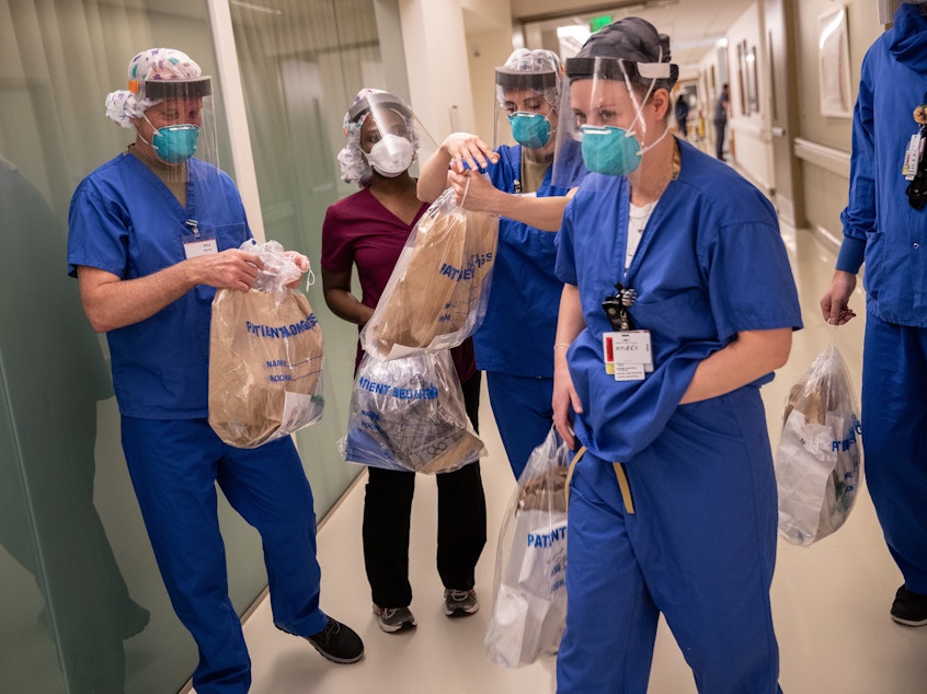 caption: Physical and occupational therapists carry bags of personal protective equipment on their way to the room of a COVID-19 patient in a Stamford Hospital intensive care unit in Stamford, Conn., on April 24. This "prone team" turns over COVID-19 to help them breathe.
