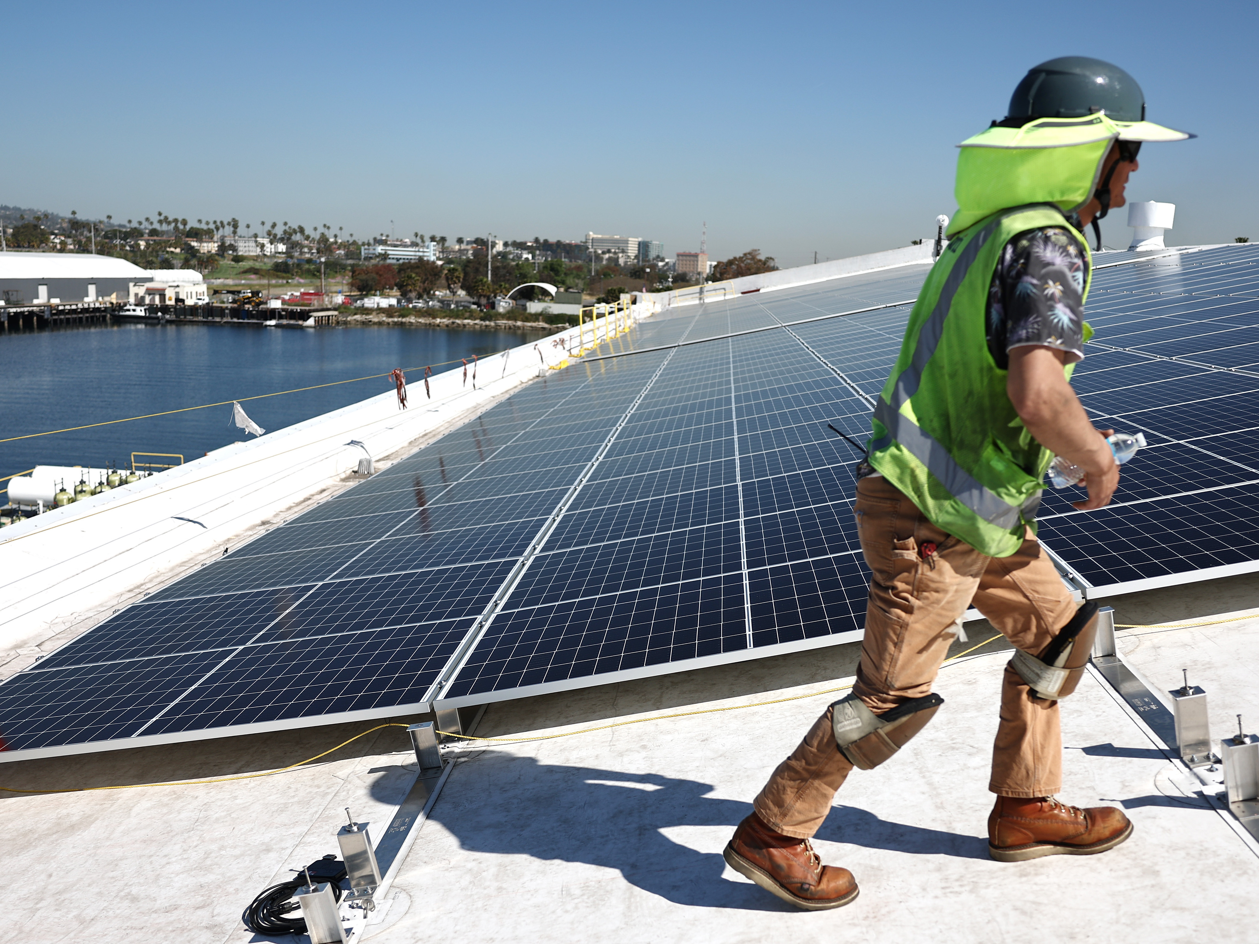 caption: Workers install solar panels on a rooftop at AltaSea's research and development facility at the Port of Los Angeles on April 21, 2023.