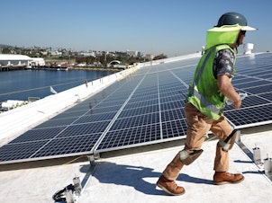caption: Workers install solar panels on a rooftop at AltaSea's research and development facility at the Port of Los Angeles on April 21, 2023.