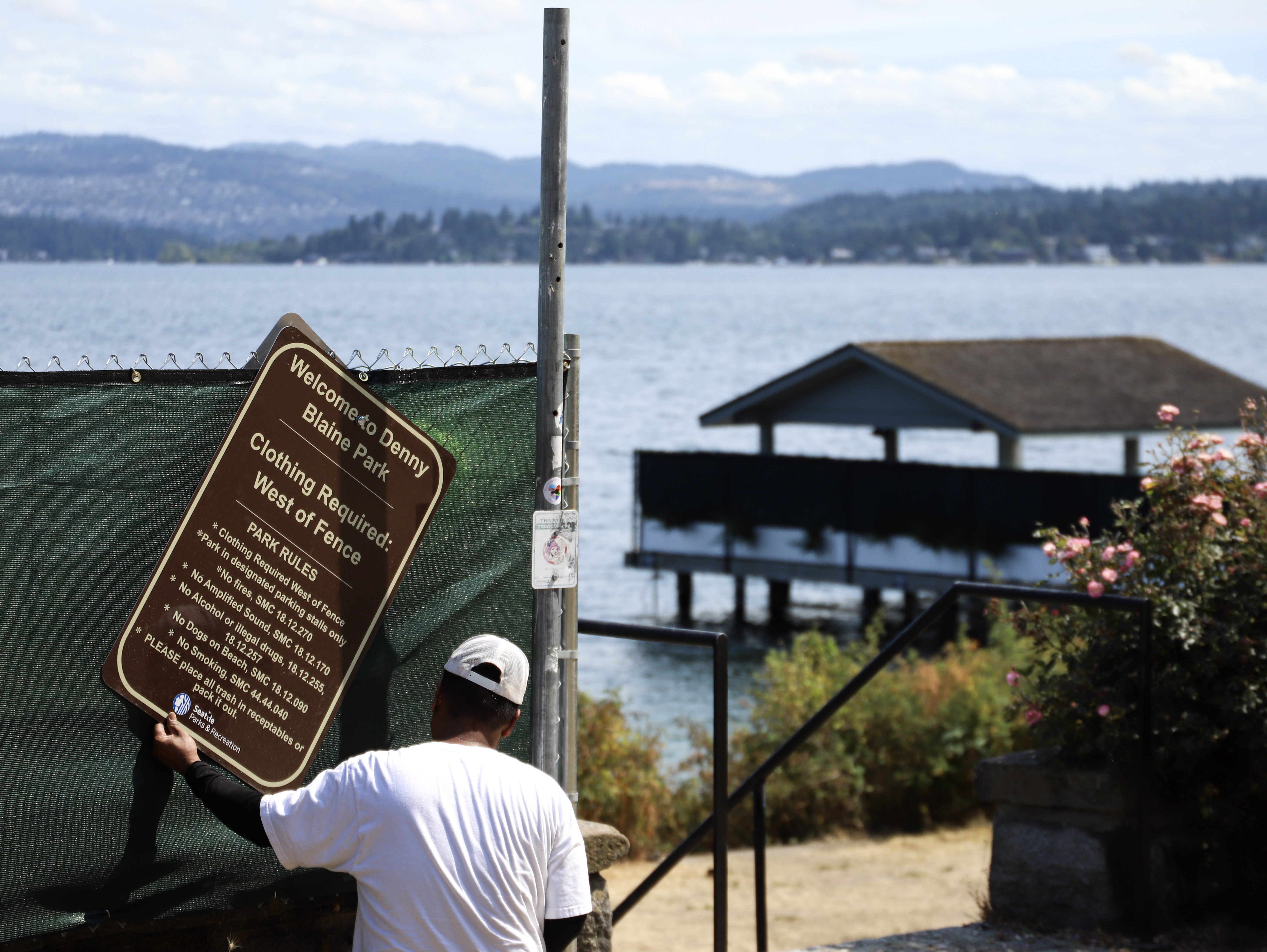 caption: A Seattle Parks worker positions a new sign explaining the new division of Denny Blaine Park between clothing required and clothing optional sections. 