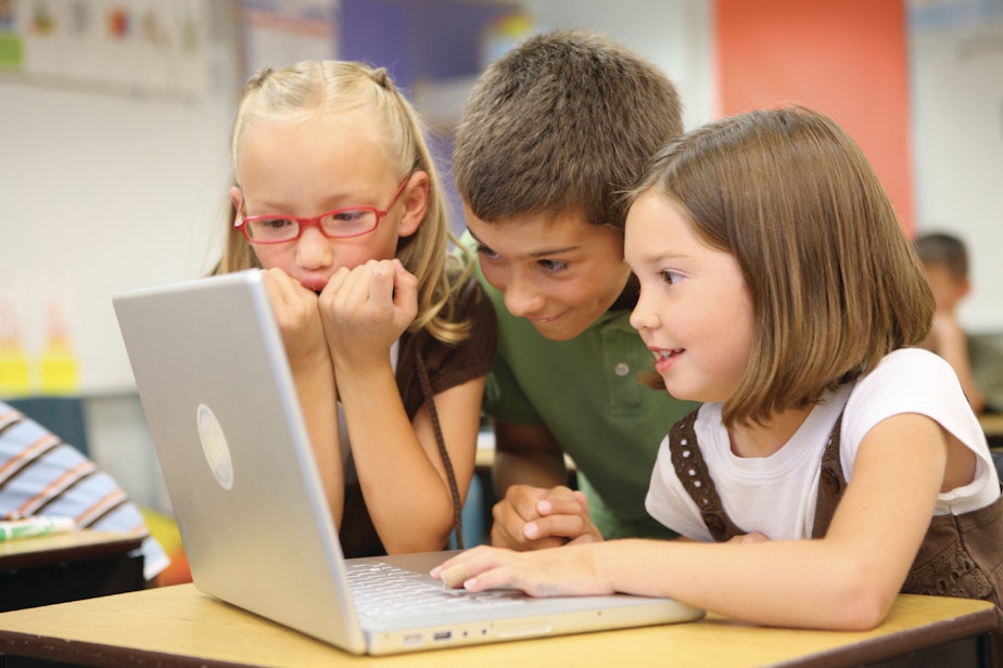 Three kids look on at a computer together