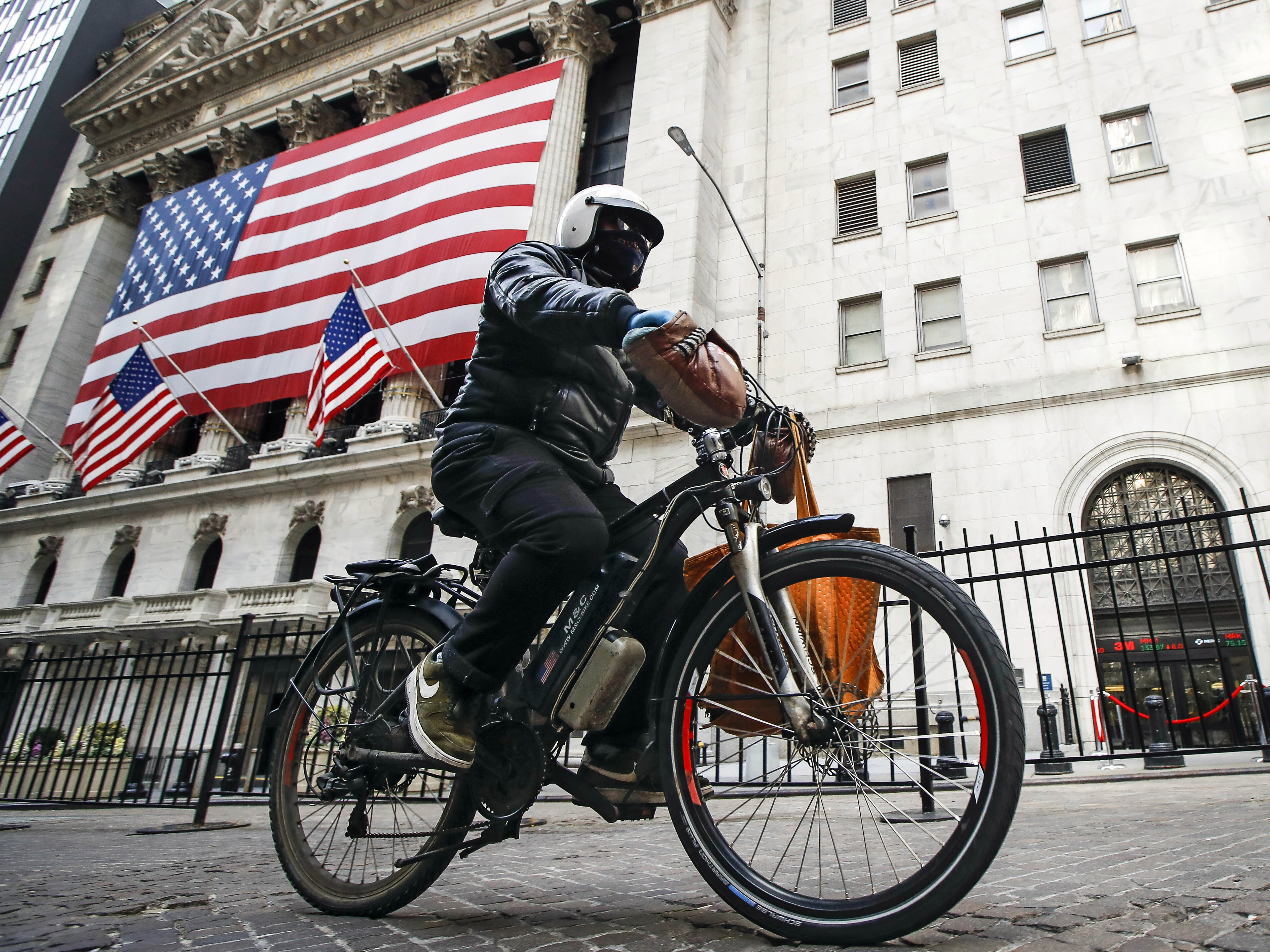 caption: A delivery worker rides his electric bicycle past the New York Stock Exchange on March 16, 2020, in New York. Electric bicycles and scooters are being blamed in an increasing number of fires resulting in injuries and deaths in New York City.