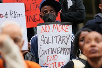 caption: People gather for a rally to protest conditions at New York City's Rikers Island jail in October of 2022. The New York City Council voted Wednesday to ban most uses of solitary confinement in the city's jails.