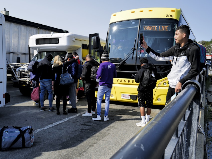 caption: Venezuelan migrants gather at the Vineyard Haven ferry terminal in Marthas Vineyard. The group was transported to Joint Base Cape Cod in Buzzards Bay.