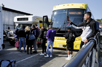 caption: Venezuelan migrants gather at the Vineyard Haven ferry terminal in Marthas Vineyard. The group was transported to Joint Base Cape Cod in Buzzards Bay.