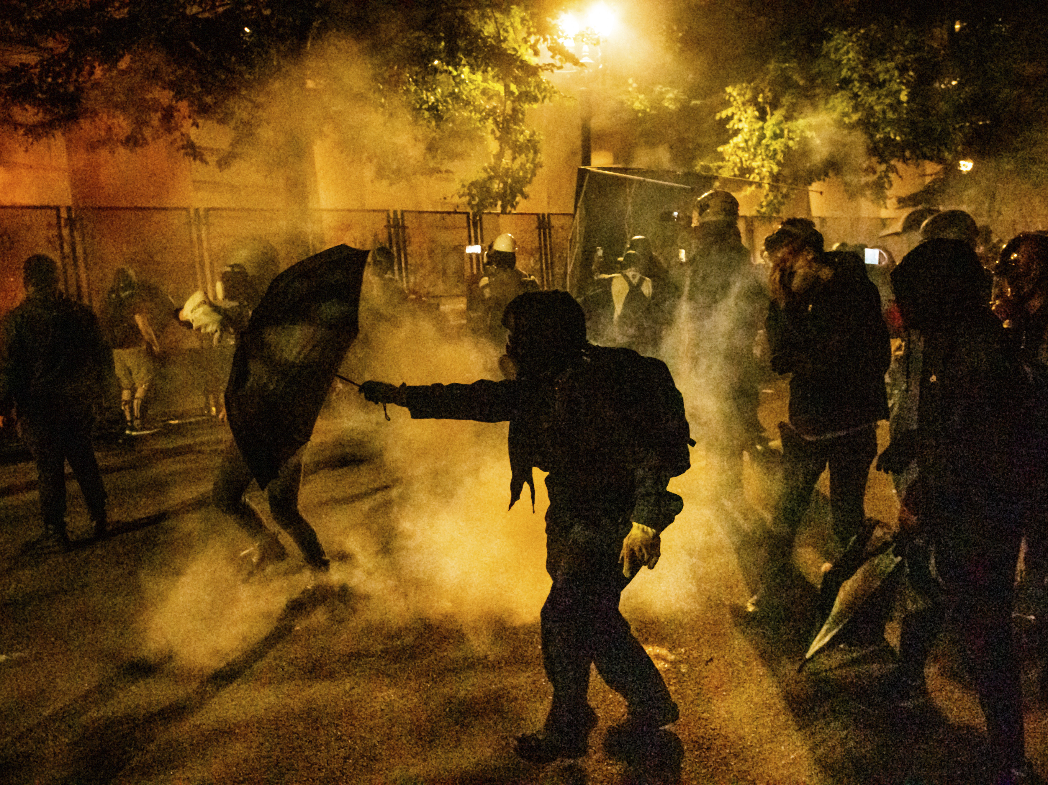 caption: Protesters walk through chemical irritants deployed by federal agents in Portland, Ore. The inspector general of the Justice Department says he is investigating federal officers' roles in responding to protests in Portland and Washington, D.C.